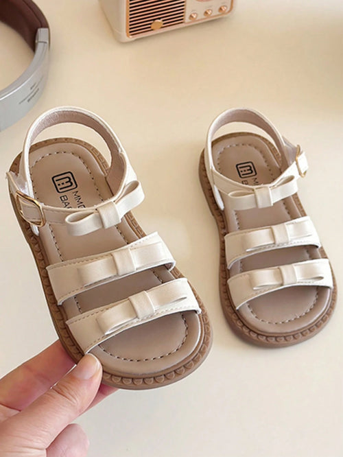 This Beige Children's Sandal Features Multiple Straps And A Bow Decoration, With A Metal Buckle Design For A Refined Touch. The Sole Is In A Brown Color. The Sweet And Cute Style Belongs To The Summer
