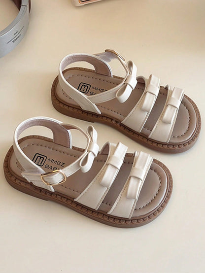 This Beige Children's Sandal Features Multiple Straps And A Bow Decoration, With A Metal Buckle Design For A Refined Touch. The Sole Is In A Brown Color. The Sweet And Cute Style Belongs To The Summer