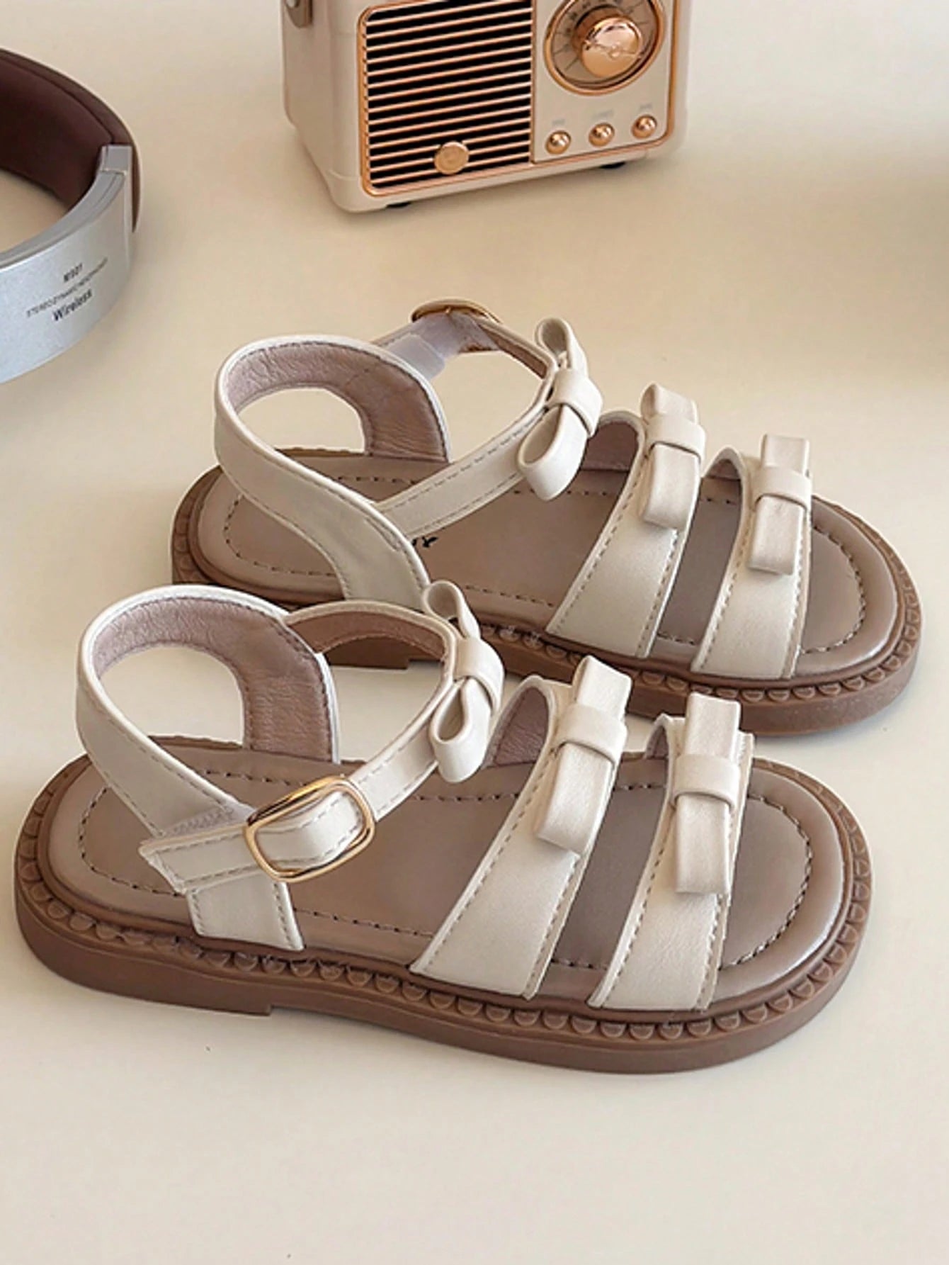 This Beige Children's Sandal Features Multiple Straps And A Bow Decoration, With A Metal Buckle Design For A Refined Touch. The Sole Is In A Brown Color. The Sweet And Cute Style Belongs To The Summer
