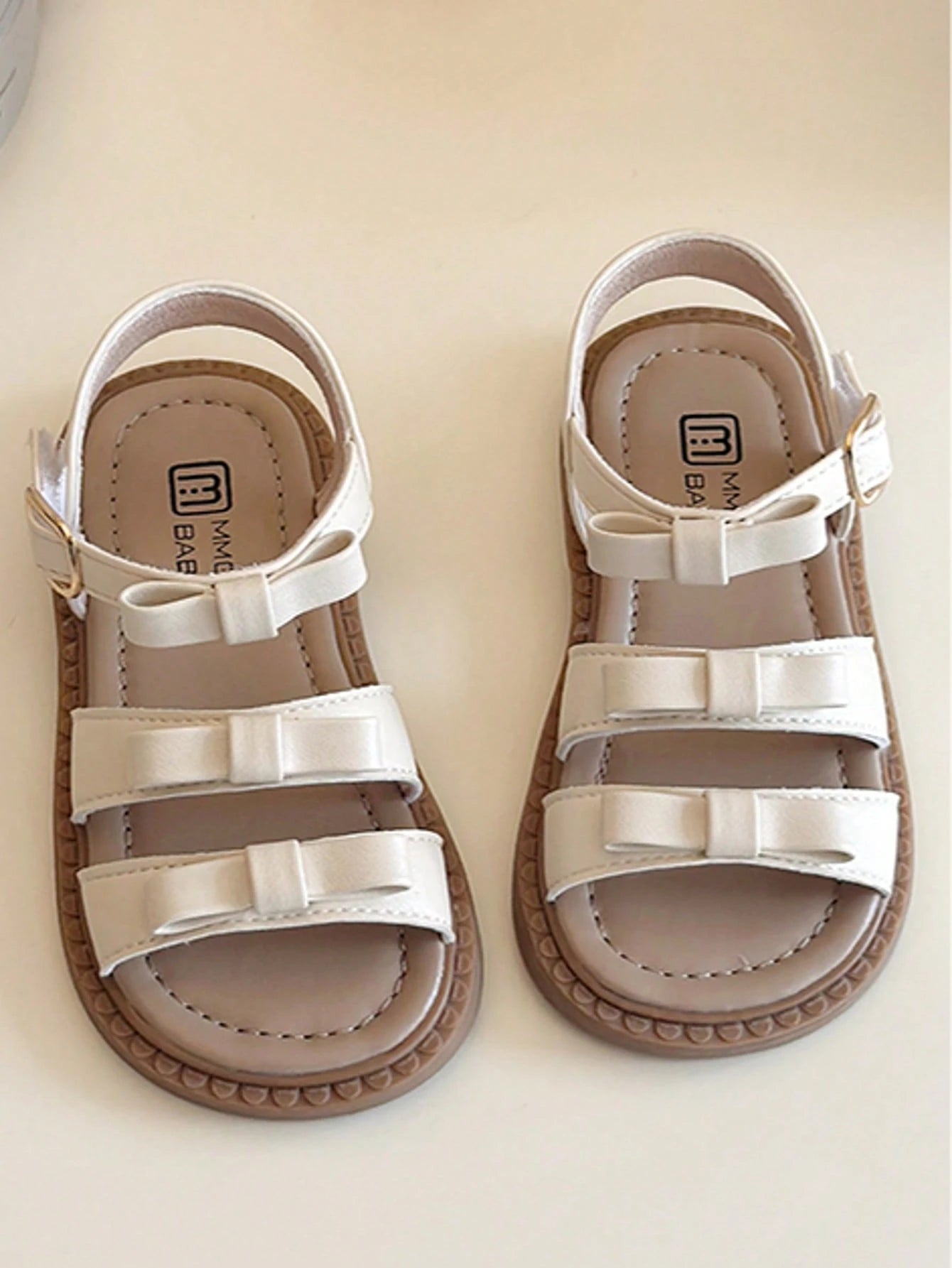 This Beige Children's Sandal Features Multiple Straps And A Bow Decoration, With A Metal Buckle Design For A Refined Touch. The Sole Is In A Brown Color. The Sweet And Cute Style Belongs To The Summer