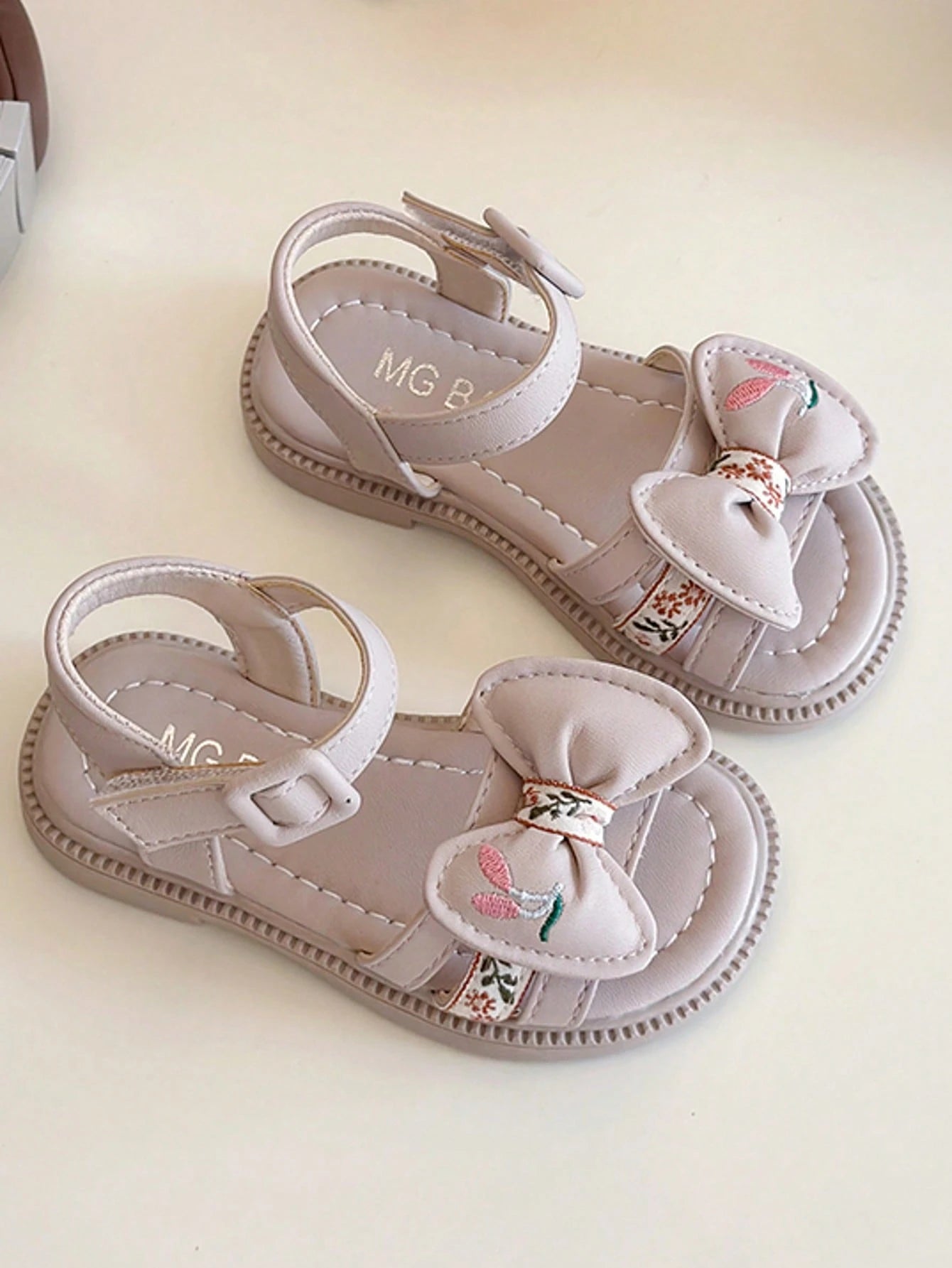 This Beige Children's Sandal Features Multiple Straps And A Bow Decoration, With A Metal Buckle Design For A Refined Touch. The Sole Is In A Brown Color. The Sweet And Cute Style Belongs To The Summer