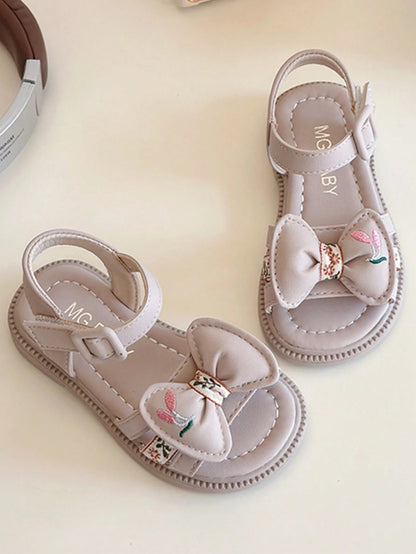 This Beige Children's Sandal Features Multiple Straps And A Bow Decoration, With A Metal Buckle Design For A Refined Touch. The Sole Is In A Brown Color. The Sweet And Cute Style Belongs To The Summer